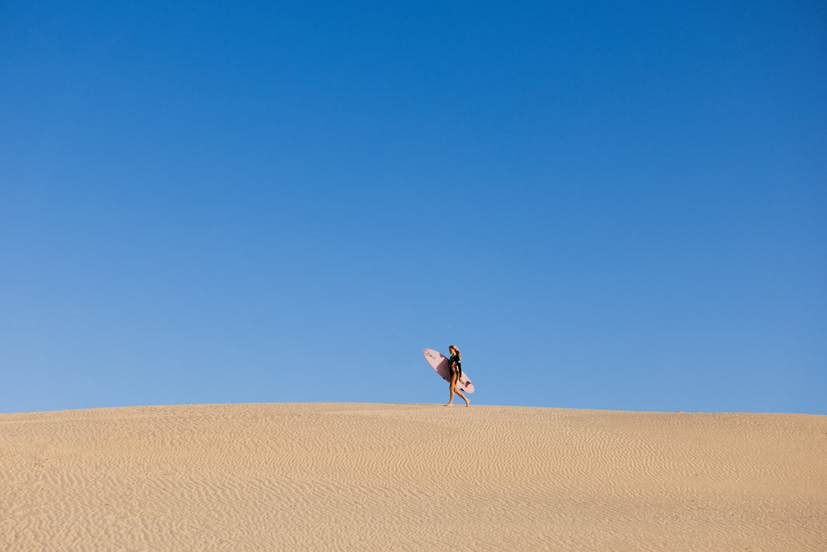 Surfista con su tabla caminando por una duna