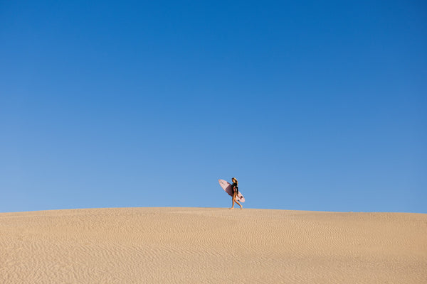 Surfista con su tabla caminando por una duna